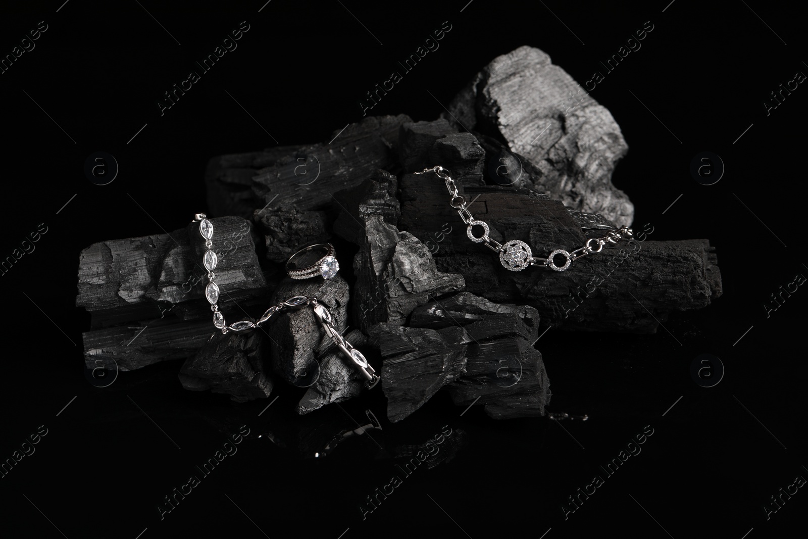 Photo of Luxury jewelry. Stylish presentation of elegant ring and bracelets on coal against black background