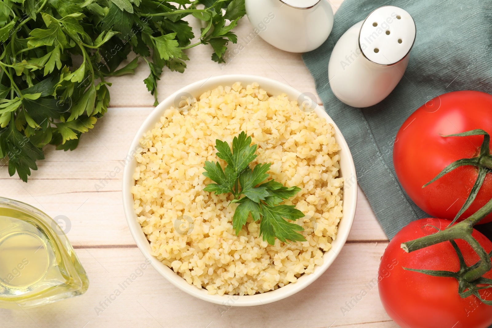 Photo of Delicious bulgur with parsley in bowl, tomatoes and oil on wooden table, top view