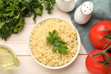 Delicious bulgur with parsley in bowl, tomatoes and oil on wooden table, top view