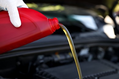 Photo of Man pouring motor oil from red container against blurred background, closeup
