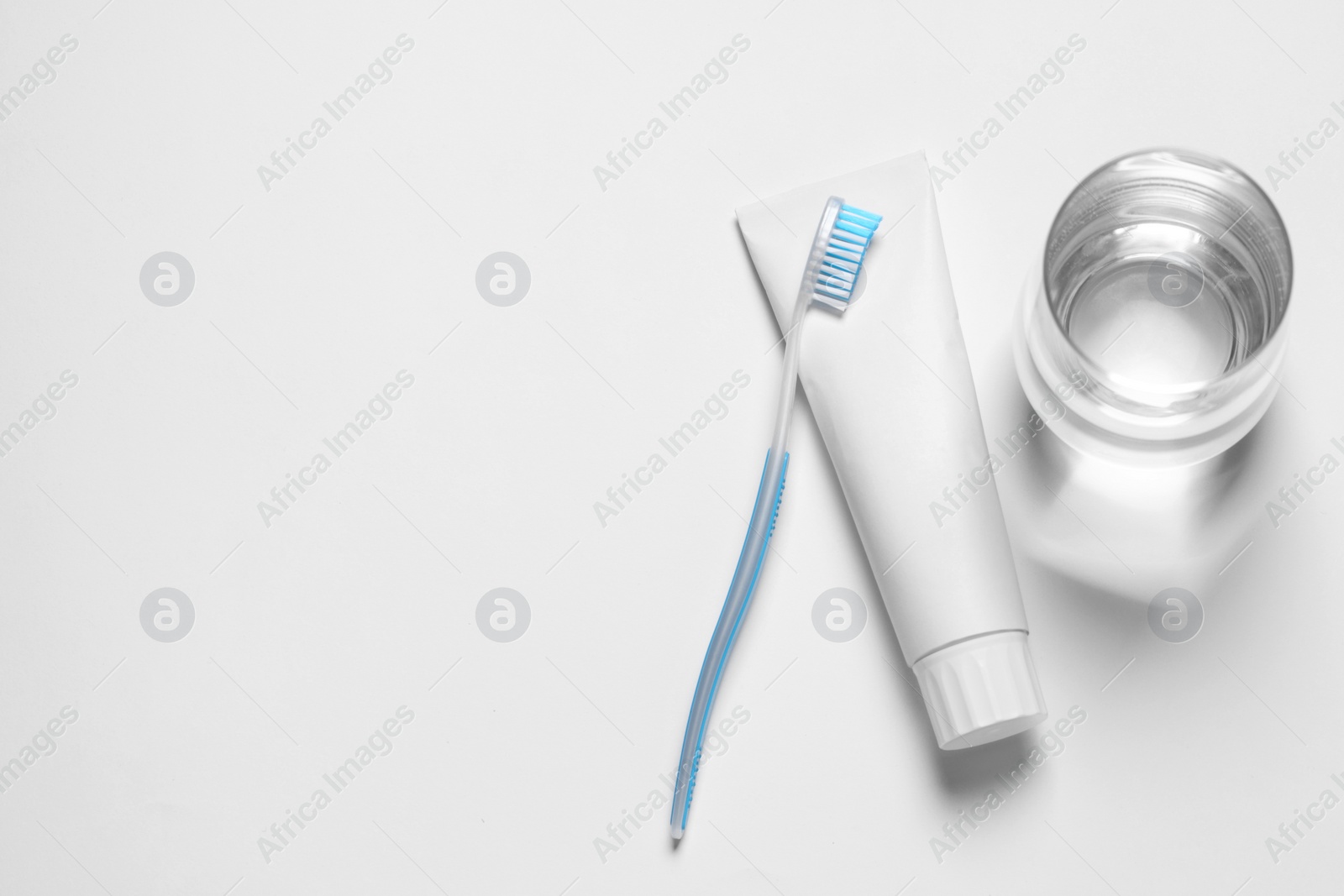 Photo of Plastic toothbrush with paste and glass of water on white background, top view. Space for text