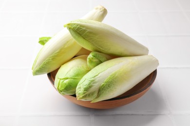 Photo of Fresh raw Belgian endives (chicory) in bowl on white tiled table