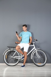 Photo of Handsome young hipster man with bicycle and phone near color wall