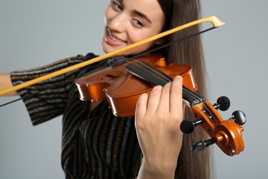 Beautiful woman playing violin on grey background, closeup