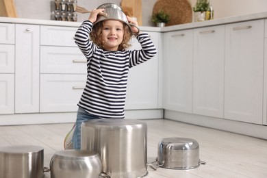 Photo of Little girl pretending to play drums on pots in kitchen