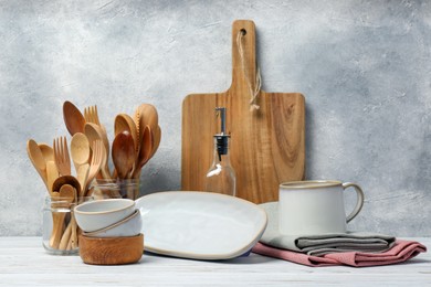 Different kitchenware and dishware on white wooden table against textured wall