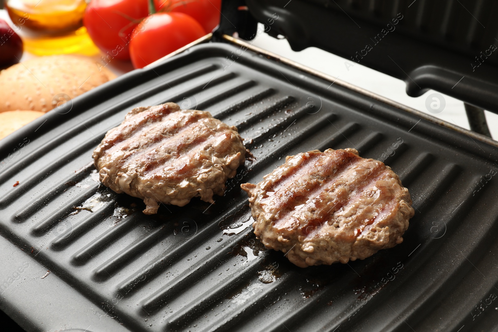 Photo of Delicious hamburger patties cooking on electric grill, closeup