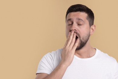 Photo of Sleepy man yawning on beige background, space for text. Insomnia problem