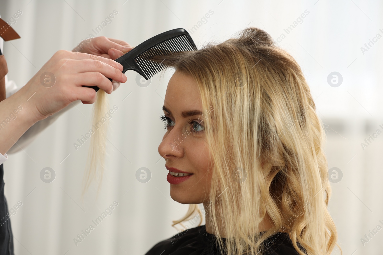 Photo of Hair styling. Professional hairdresser combing woman's hair in salon, closeup