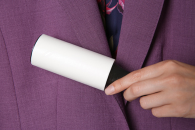 Woman cleaning purple jacket with lint roller, closeup