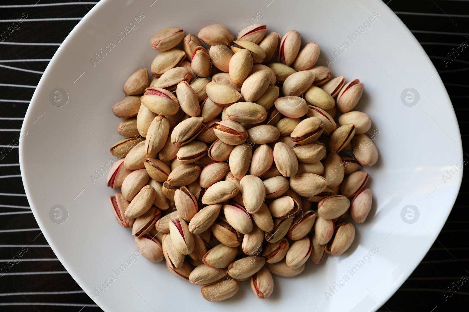 Photo of Many tasty pistachios on black table, top view