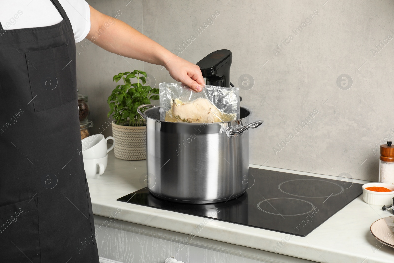 Photo of Woman taking out vacuum packed meat from pot in kitchen, closeup. Thermal immersion circulator for sous vide cooking