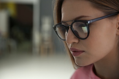 Photo of Young woman wearing glasses on blurred background, closeup. Ophthalmology service