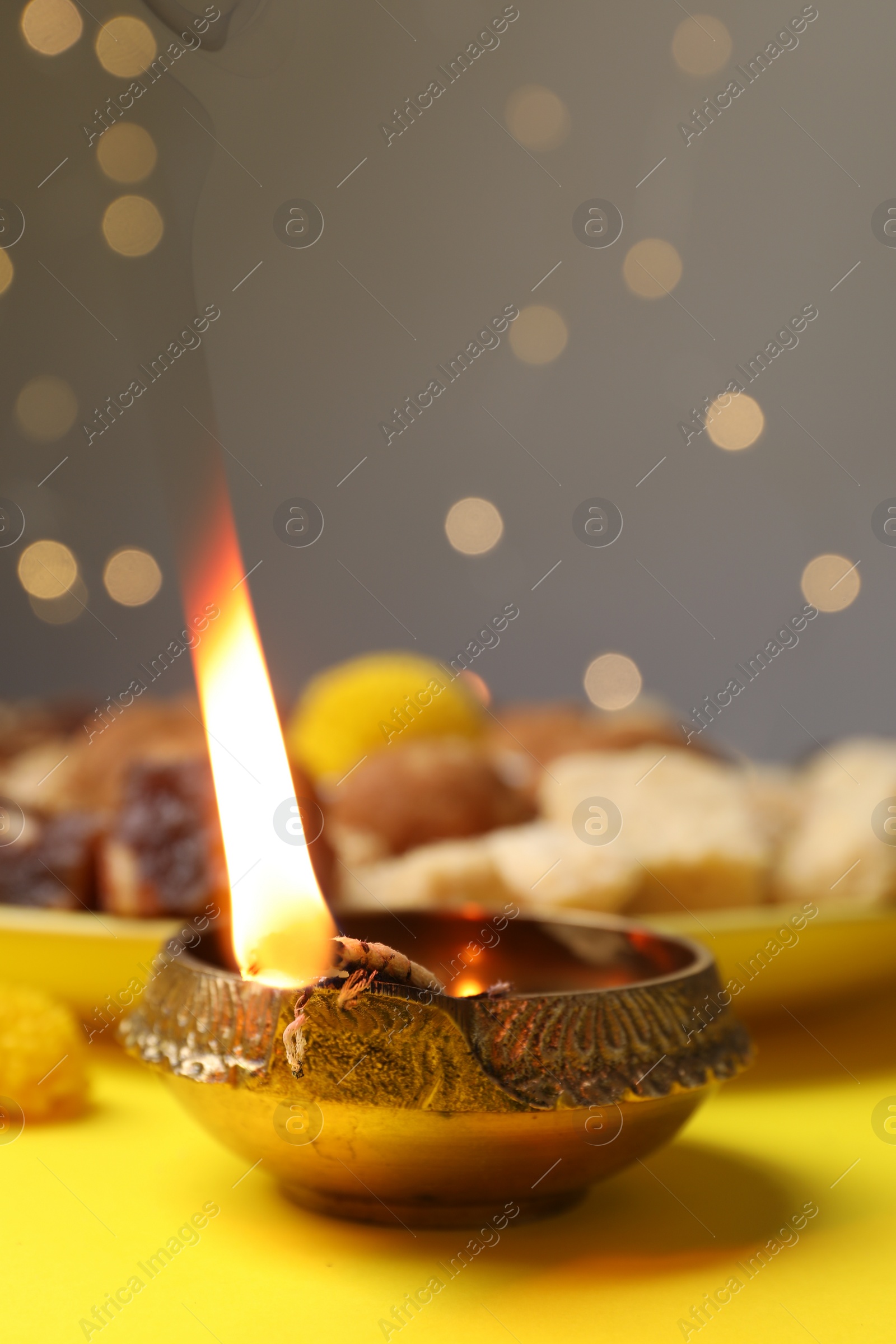 Photo of Happy Diwali. Diya lamp on yellow table against blurred lights, closeup