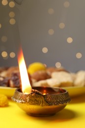 Happy Diwali. Diya lamp on yellow table against blurred lights, closeup