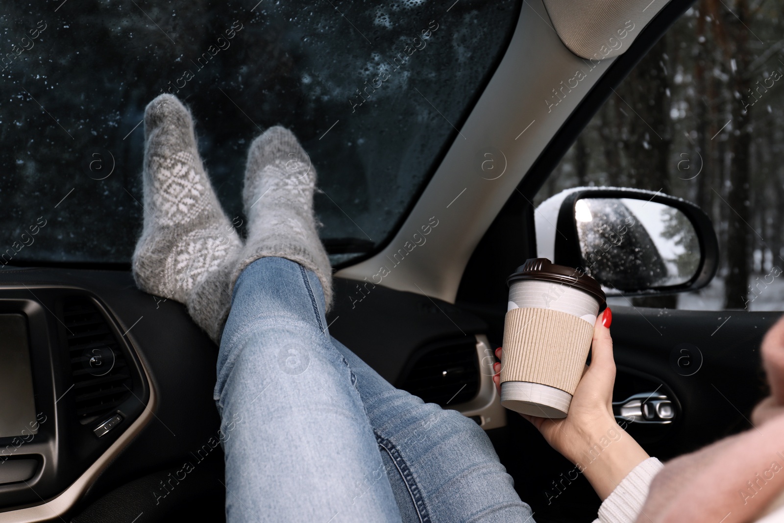 Photo of Young woman in warm socks with coffee resting inside car, closeup