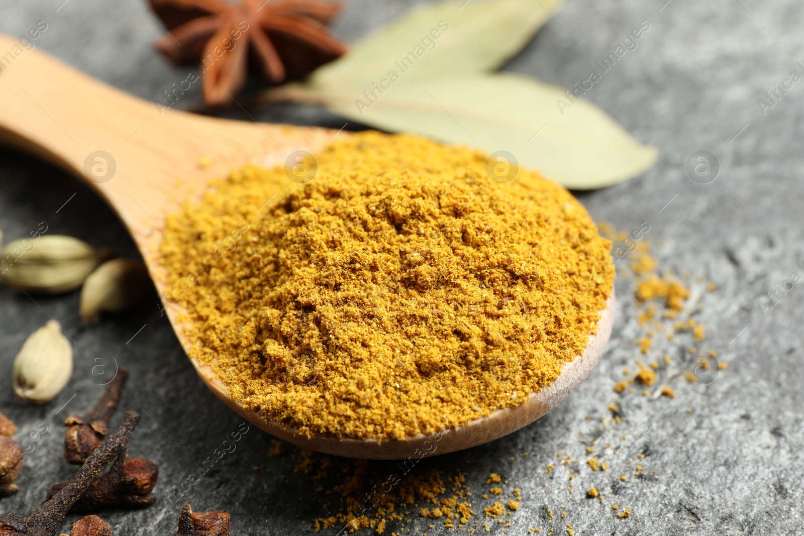 Photo of Spoon with dry curry powder and other spices on dark textured table, closeup
