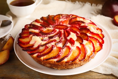 Photo of Delicious cake with plums on wooden table