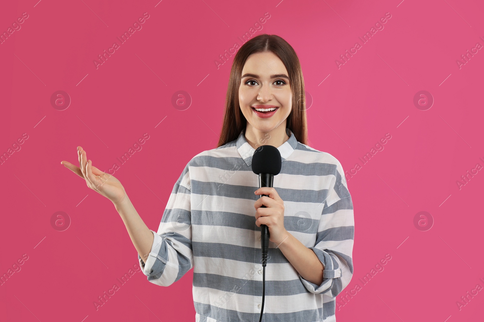 Photo of Young female journalist with microphone on pink background