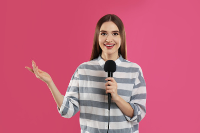 Young female journalist with microphone on pink background