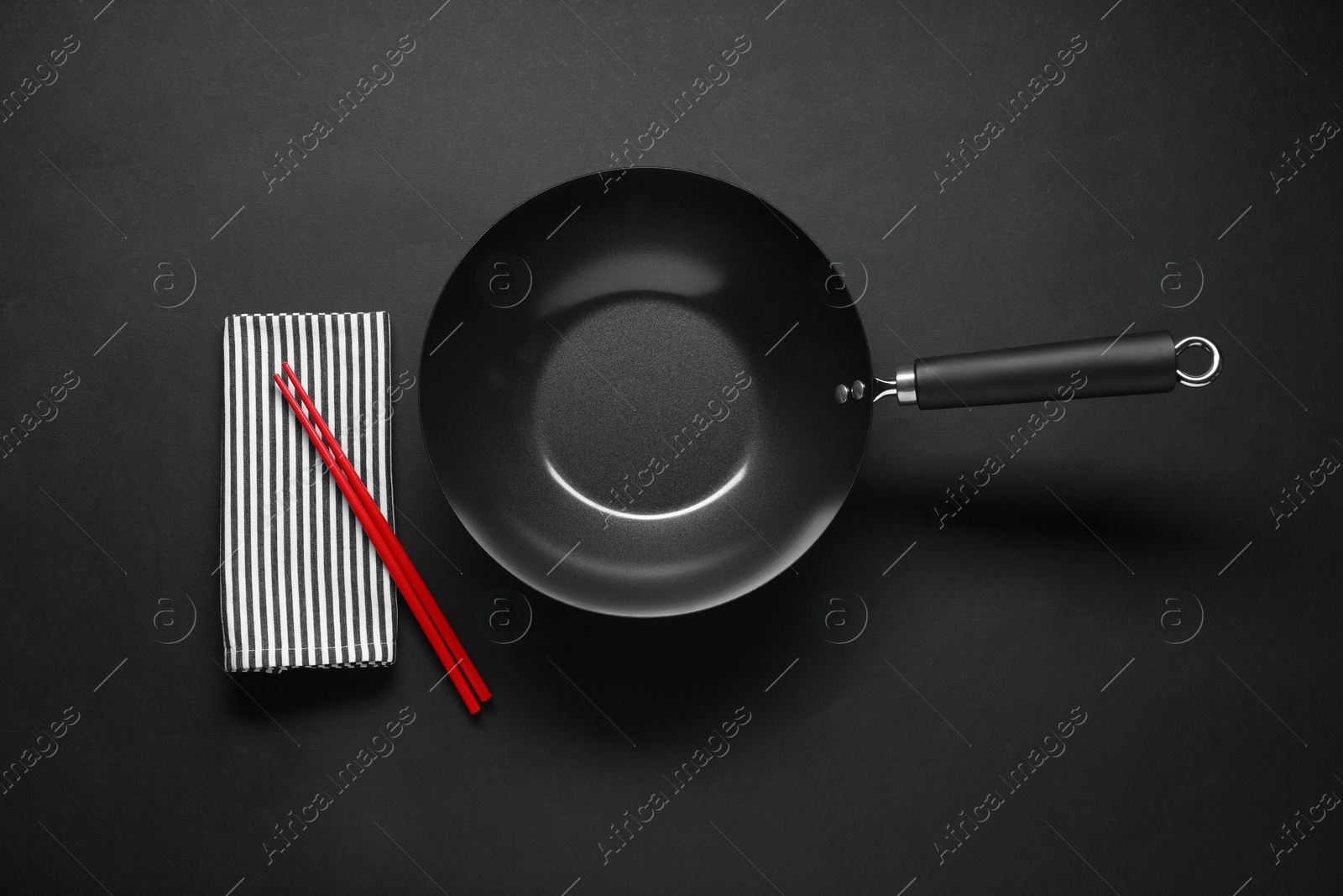 Photo of Empty iron wok and chopsticks on black table, flat lay