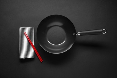 Empty iron wok and chopsticks on black table, flat lay