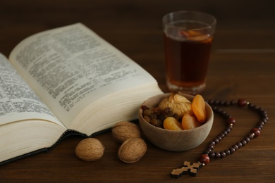 Photo of Bible, rosary beads, walnuts and dried fruits on wooden table. Lent season