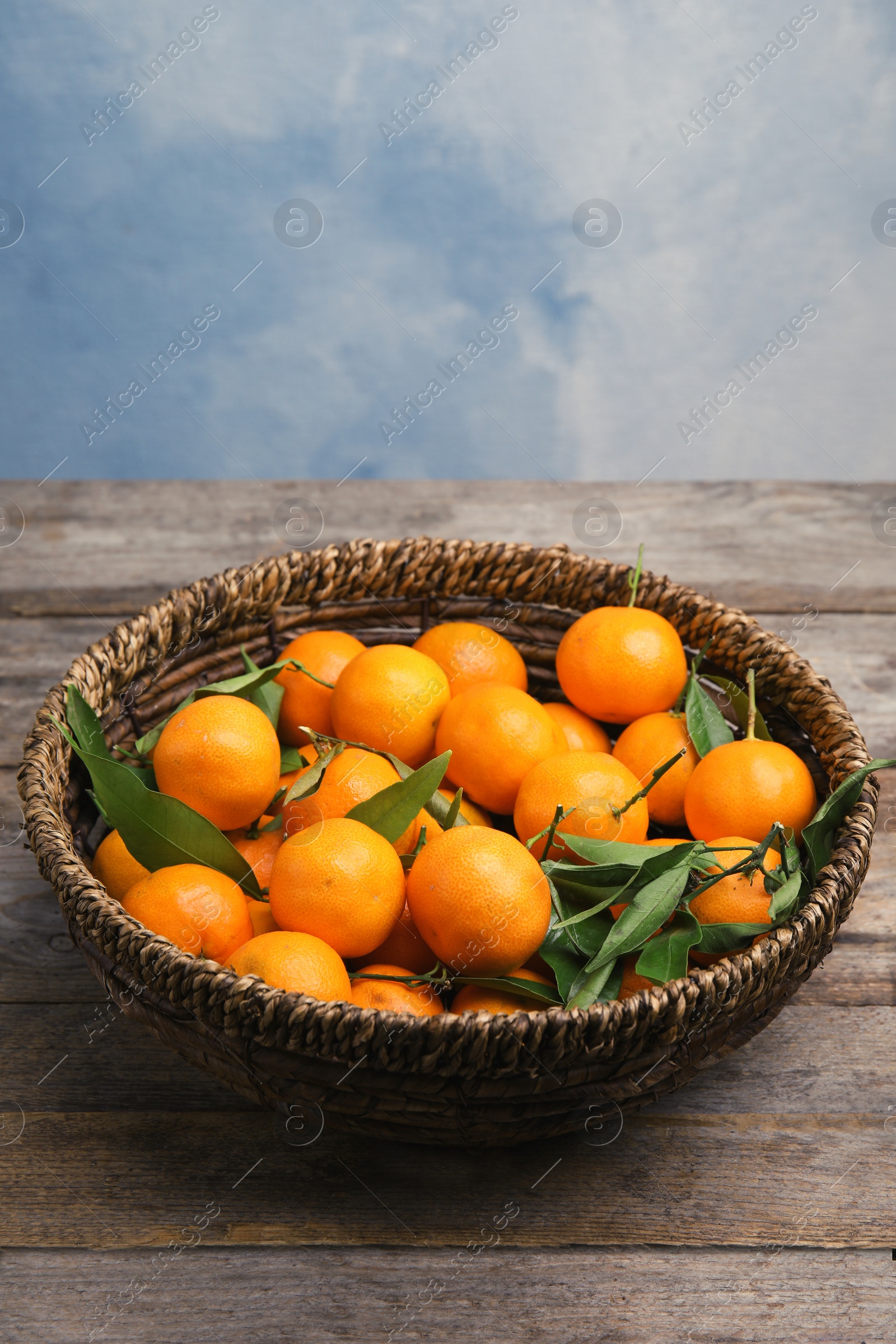 Photo of Fresh ripe tangerines in wicker basket on wooden table. Space for text