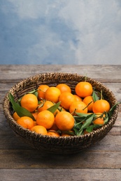 Fresh ripe tangerines in wicker basket on wooden table. Space for text