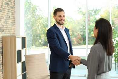 Human resources manager shaking hands with applicant during job interview in office