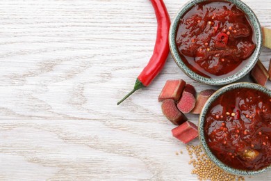 Tasty rhubarb sauce and ingredients on white wooden table, flat lay. Space for text