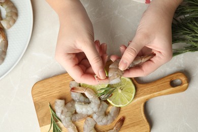 Woman peeling fresh shrimp at table, top view