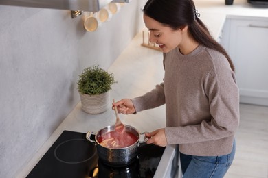 Photo of Smiling woman with wooden spoon cooking tomato soup in kitchen, above view