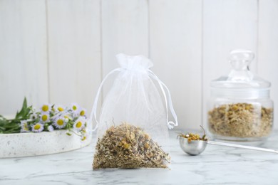 Scented sachet with dried chamomile flowers on white marble table