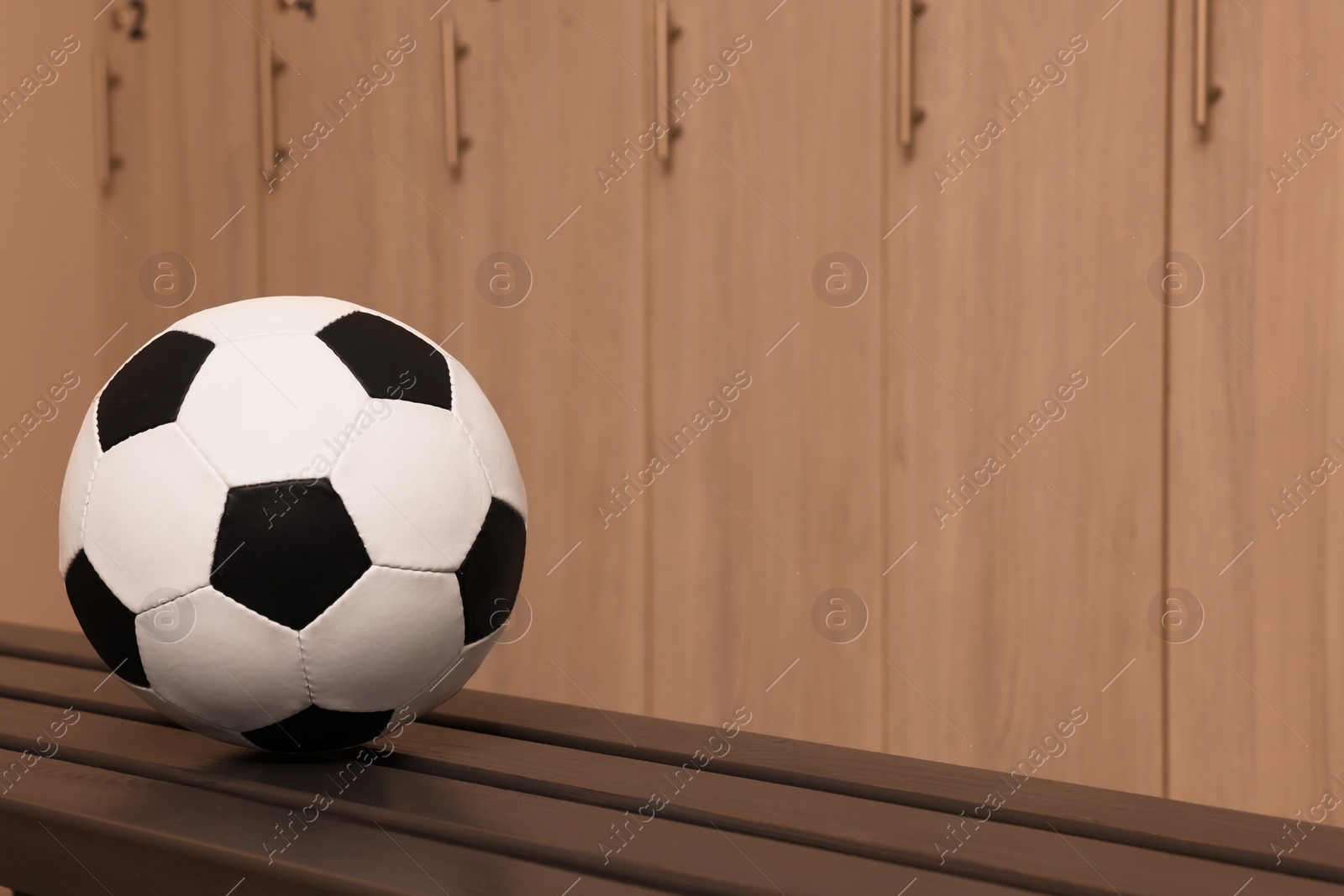 Photo of Soccer ball on wooden bench in locker room. Space for text