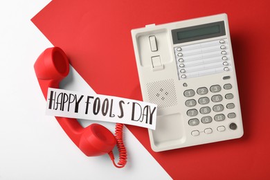 Photo of Corded phone with red handset and words Happy Fool's Day on color background, flat lay