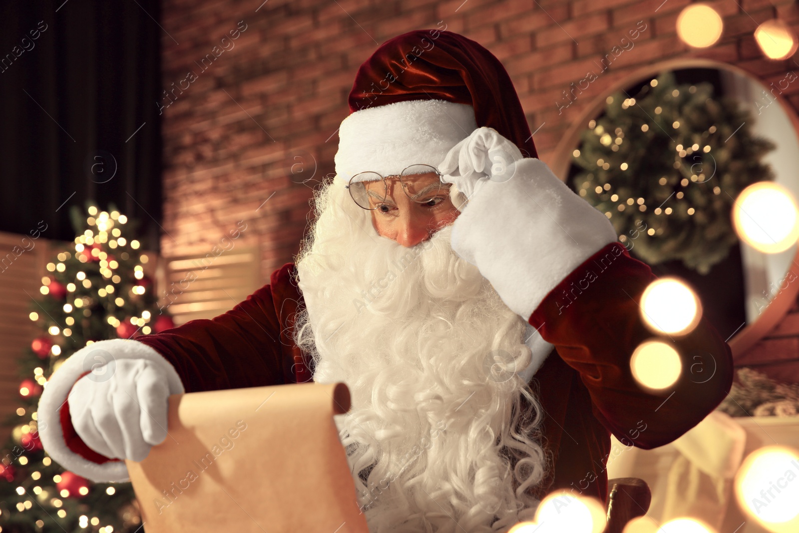 Photo of Santa Claus in glasses reading wish list indoors
