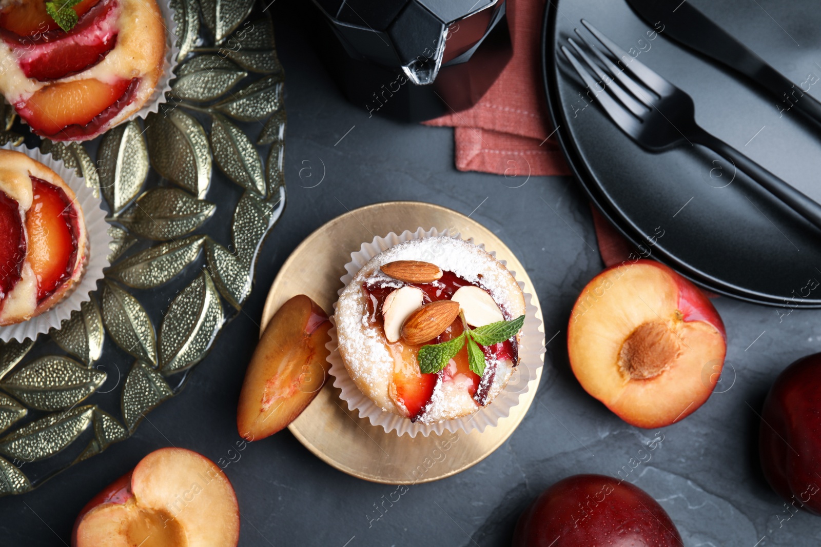 Photo of Delicious cupcakes with plums on black table, flat lay