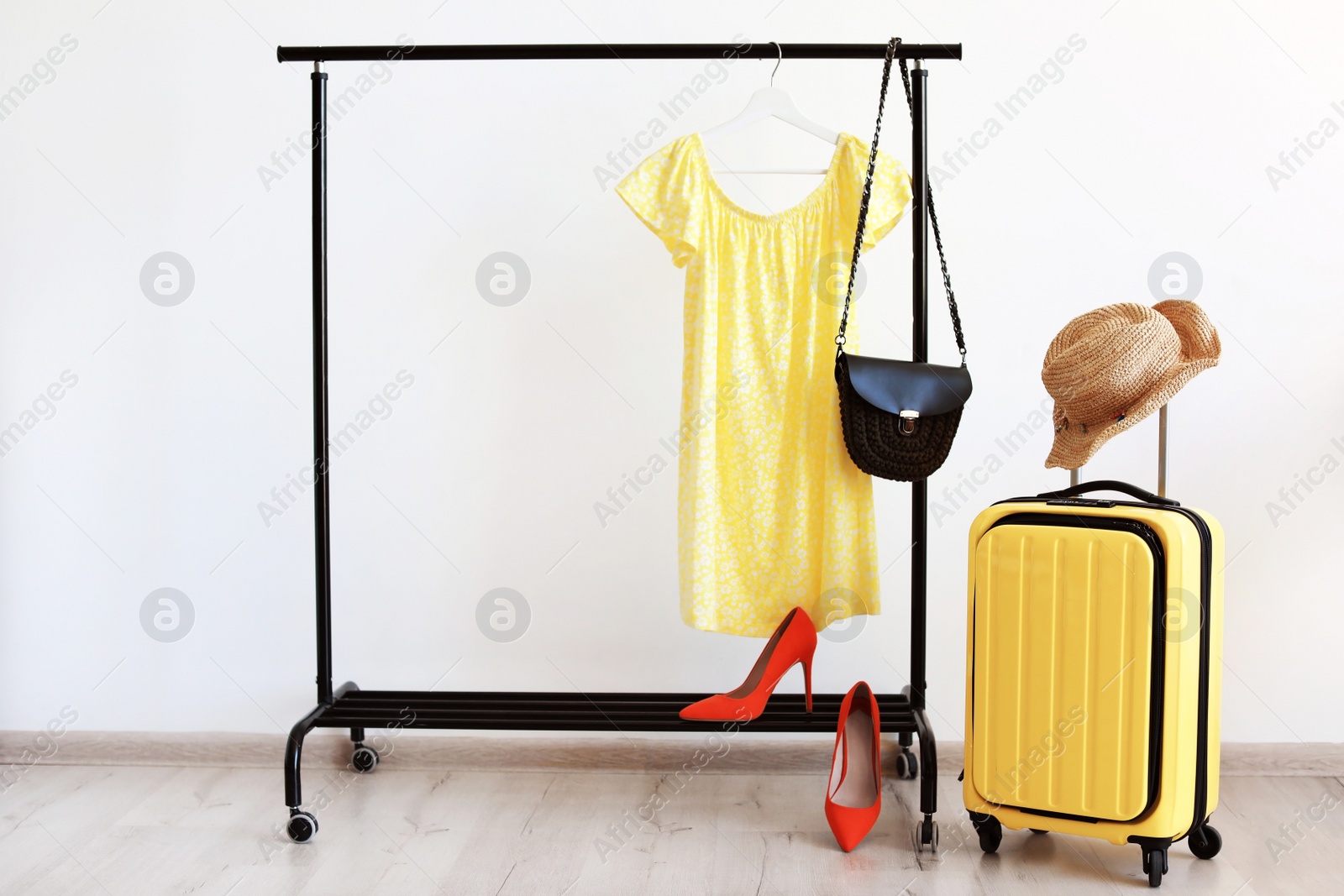 Photo of Packed yellow suitcase and rack with clothes indoors