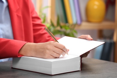 Female author signing autograph in book at table indoors, closeup