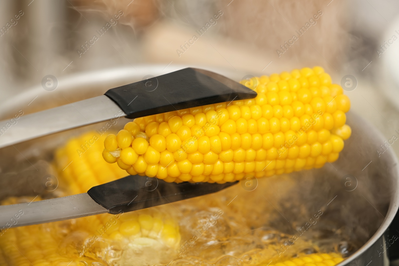 Photo of Taking corn cob from stewpot with boiling water, closeup