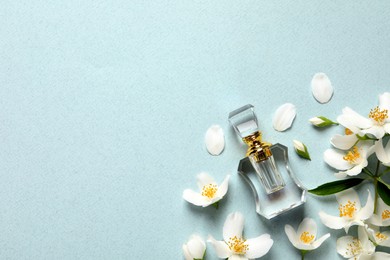 Bottle of luxury perfume and fresh jasmine flowers on light blue background, flat lay. Space for text