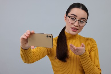 Photo of Young woman taking selfie with smartphone on grey background