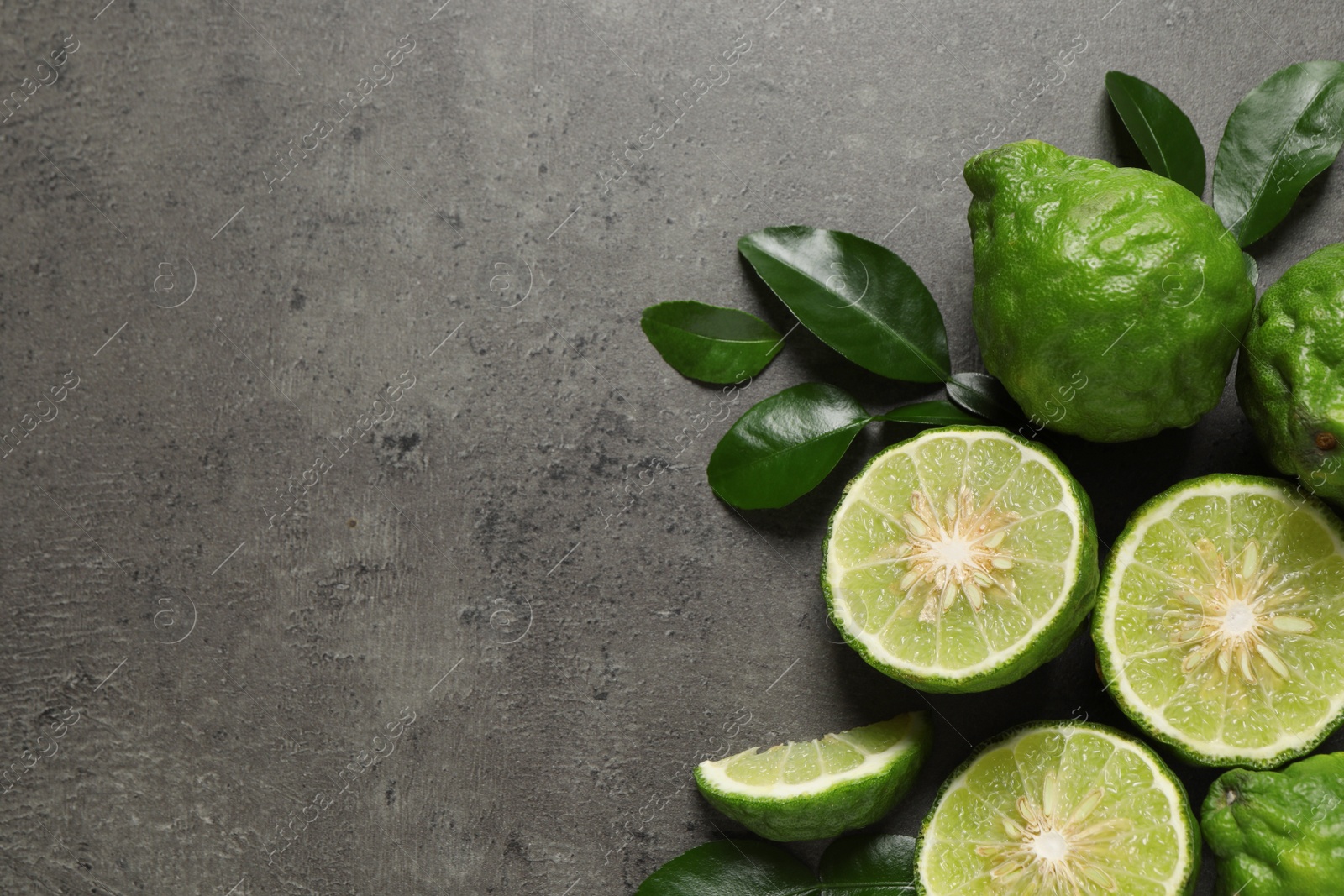 Photo of Fresh ripe bergamot fruits with green leaves on grey table, flat lay. Space for text