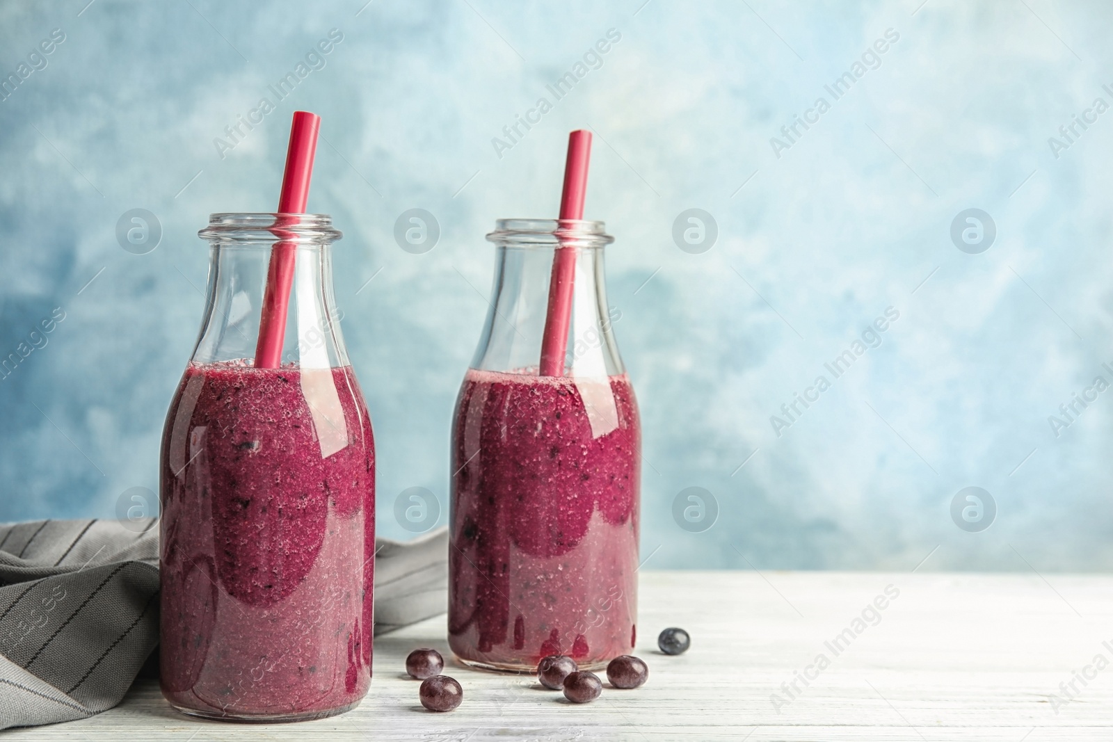 Photo of Bottles with delicious acai smoothie on table against color background