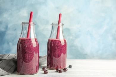 Bottles with delicious acai smoothie on table against color background