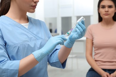 Photo of Woman waiting to get hepatitis vaccine at clinic. Doctor filling syringe from glass vial, closeup