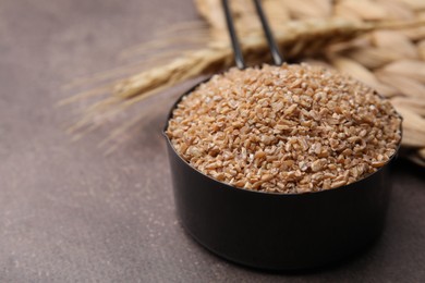 Photo of Dry wheat groats in scoop on brown table, closeup. Space for text