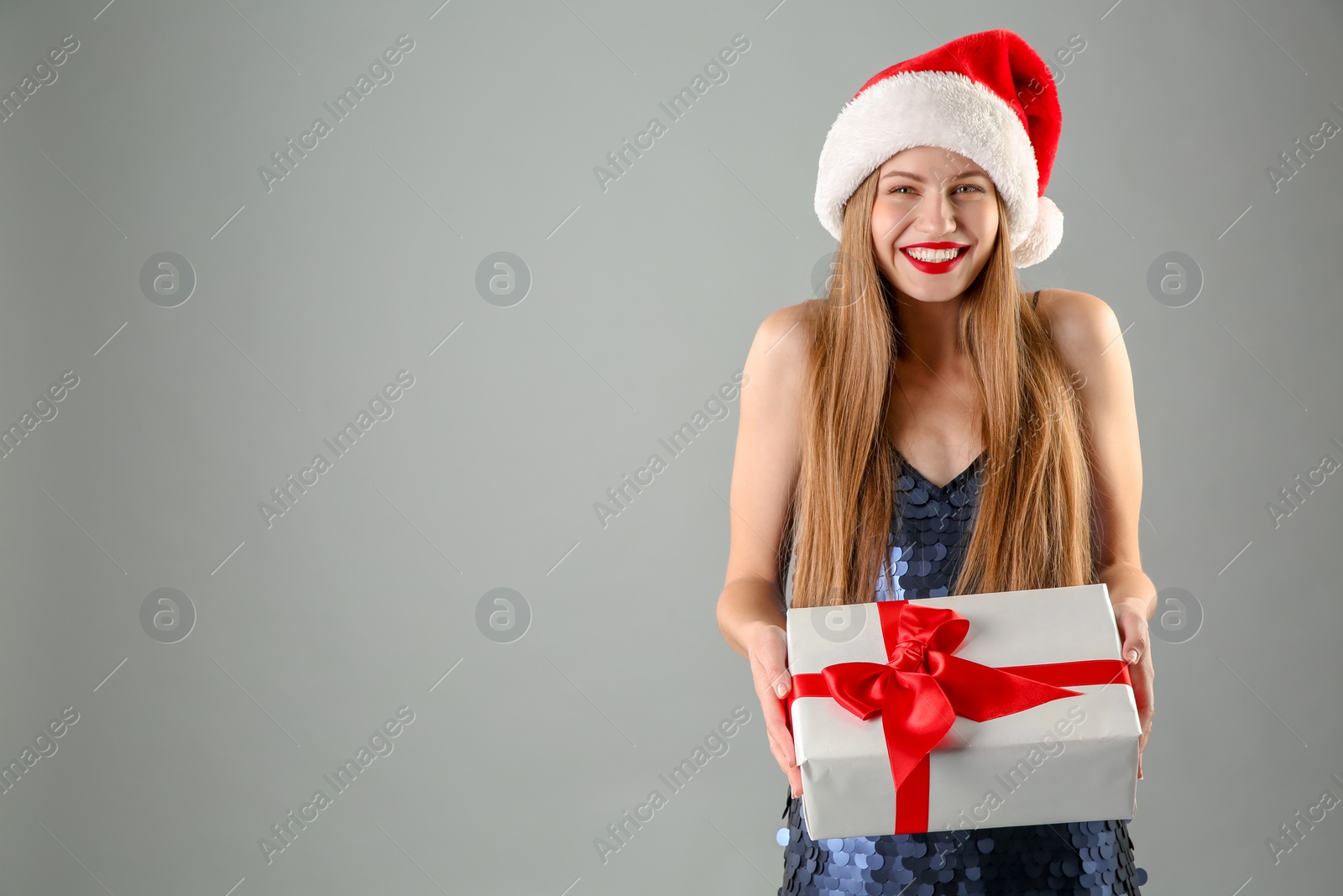 Photo of Young beautiful woman in Santa hat with gift box on grey background. Christmas celebration