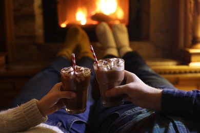 Couple with glasses of hot cocoa near fireplace at home, closeup